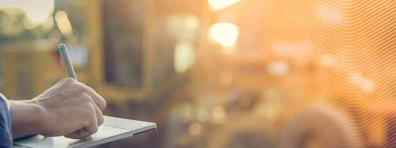 Worker in safety vest writing on a tablet at a construction site
