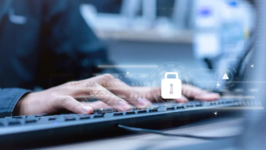Hands typing on a keyboard with digital security icons overlayed, including a padlock symbol, representing cybersecurity.