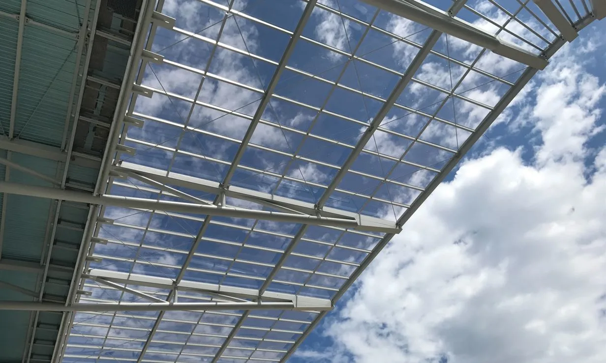 A view from below of a transparent roof structure with a cloudy blue sky visible through it.