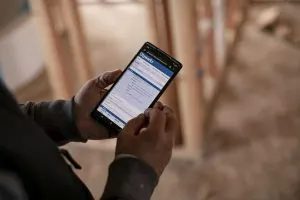 Hands holding a smartphone displaying a digital document, with a construction site in the background.