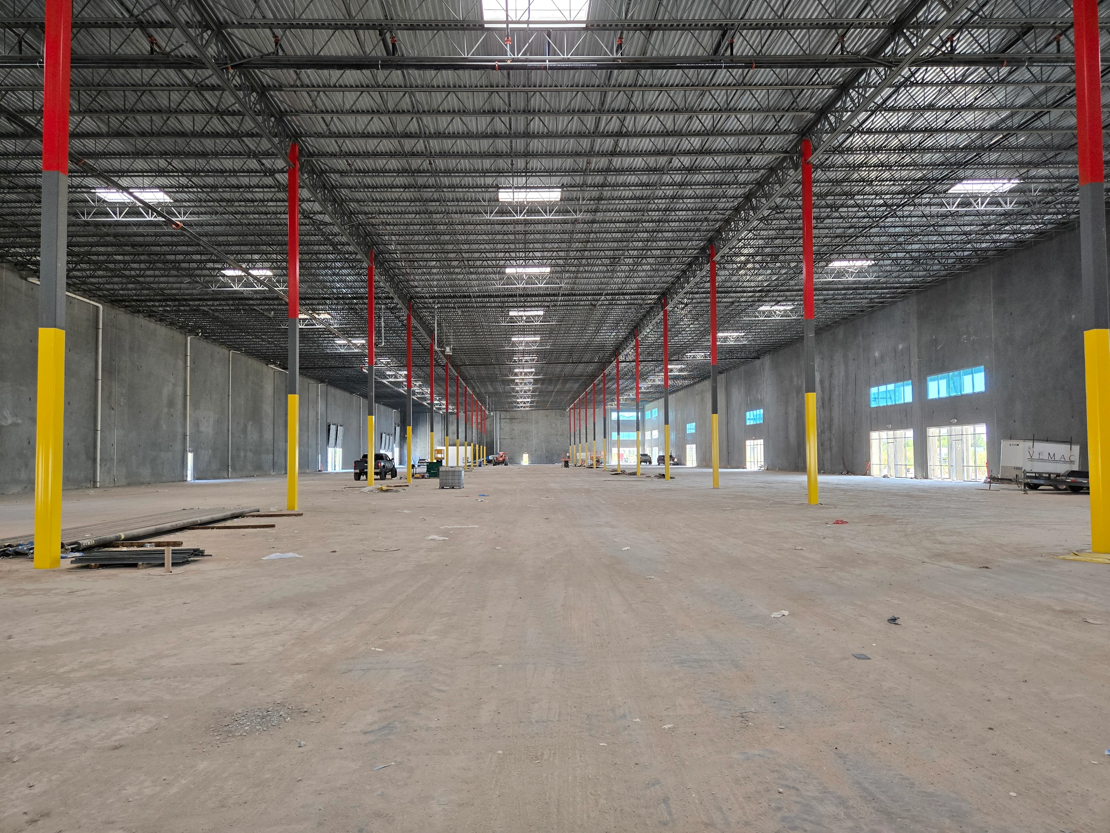 Interior of a large, empty warehouse with concrete walls, metal ceiling, and red and yellow support columns.