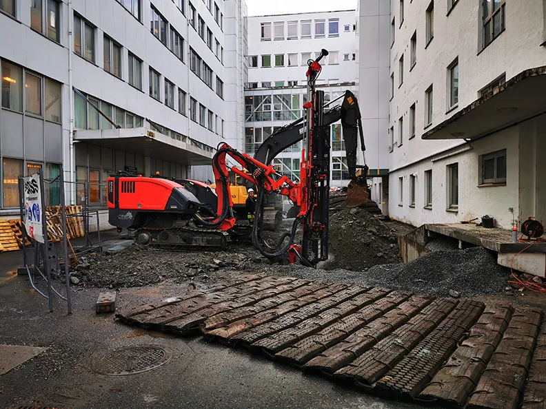 Construction site with an excavator drilling next to a building.
