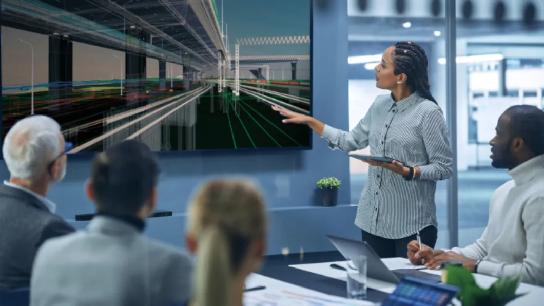 A group of people in an office conference room review the design model for a roadway or railway construction project.