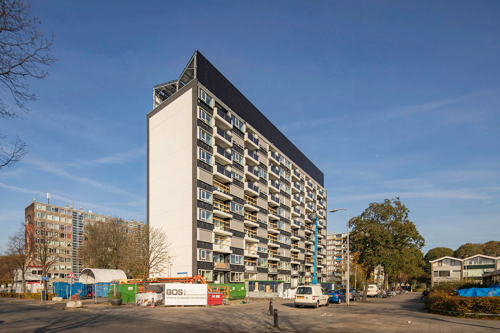 A modern apartment building with a sloped solar roof and construction site on a sunny day.