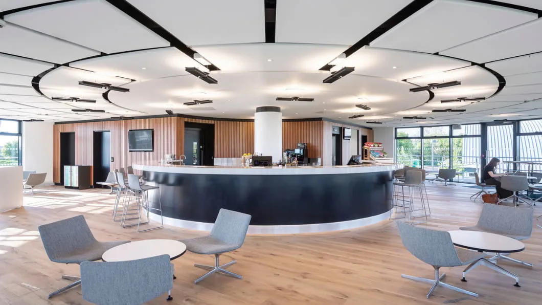 Spacious circular cafe with a large white counter, wood-paneled walls, and modern grey chairs.