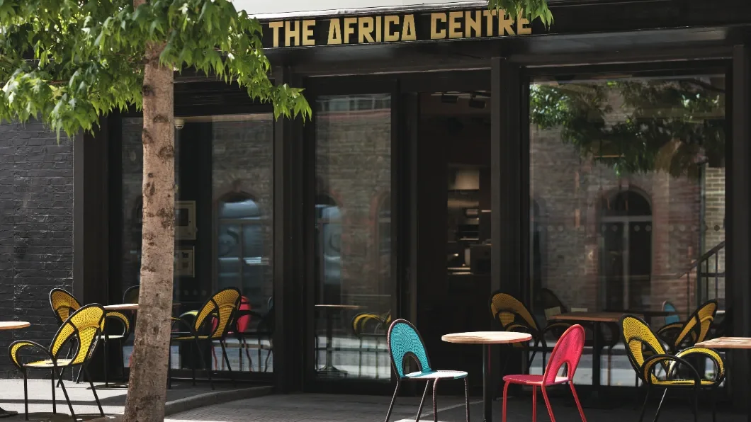 Façade extérieure de l'Africa Centre avec des tables et des chaises de différentes couleurs.