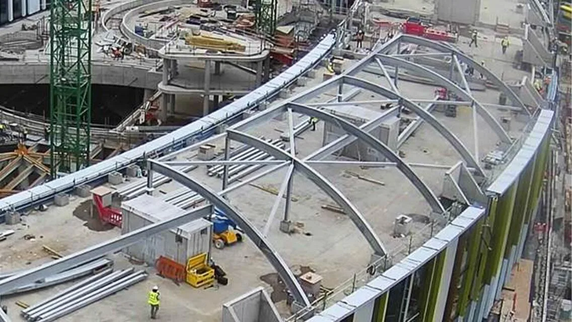 Aerial view of a large building under construction, featuring a curved steel framework roof.