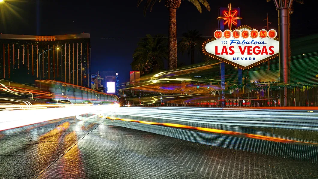 Nighttime long exposure of the "Welcome to Fabulous Las Vegas" sign with vibrant light trails and the Mandalay Bay hotel in the background.