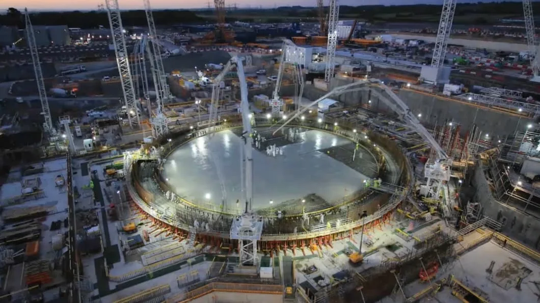 Construction site at dusk with cranes and concrete pouring into a large circular foundation.