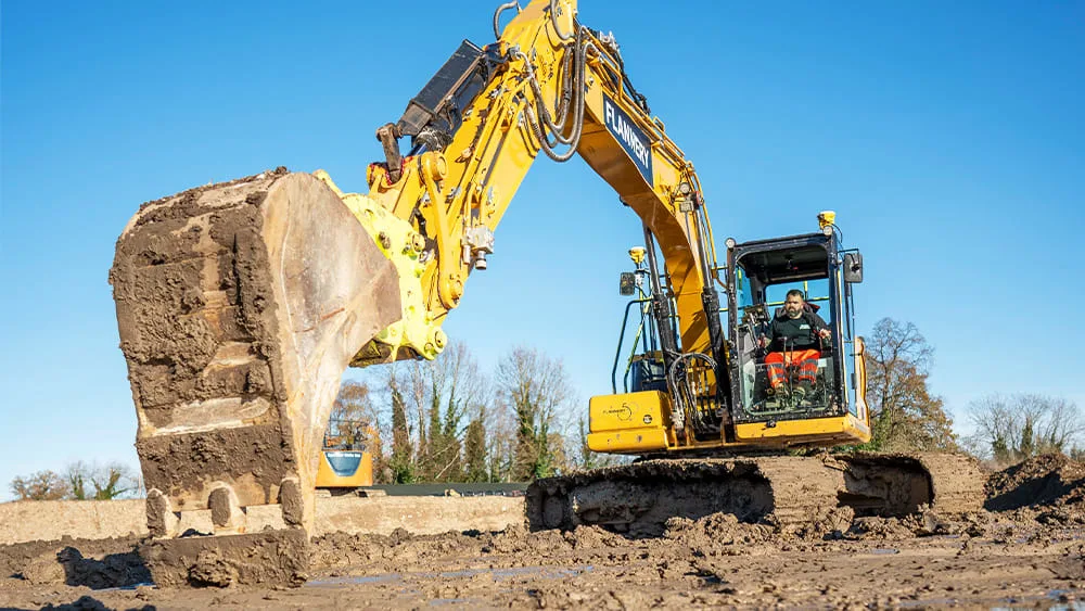 An excavator operator in the cab of a large yellow excavator.