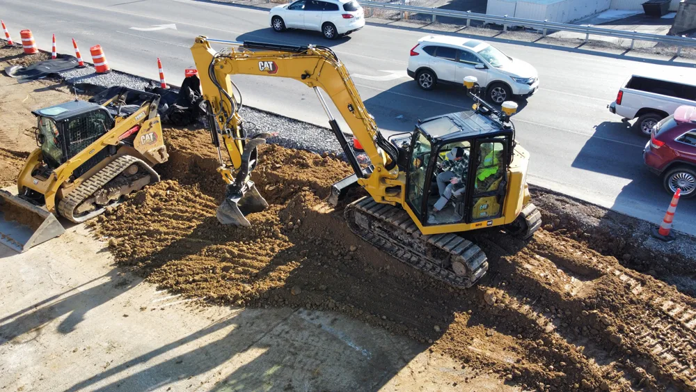 Two yellow excavators are working on a construction site next to a road with traffic.