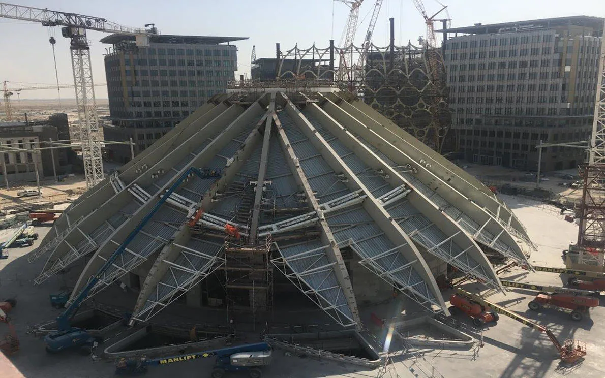 A wide shot of a large, dome-like structure under construction, with steel beams radiating from a central point.