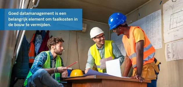 Three construction workers in hard hats and safety vests collaborate around a table with blueprints and a laptop.