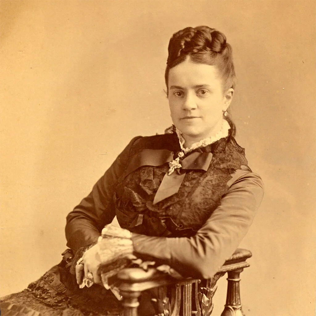 Portrait of a woman in a dark, ornate dress with lace collar and bow.