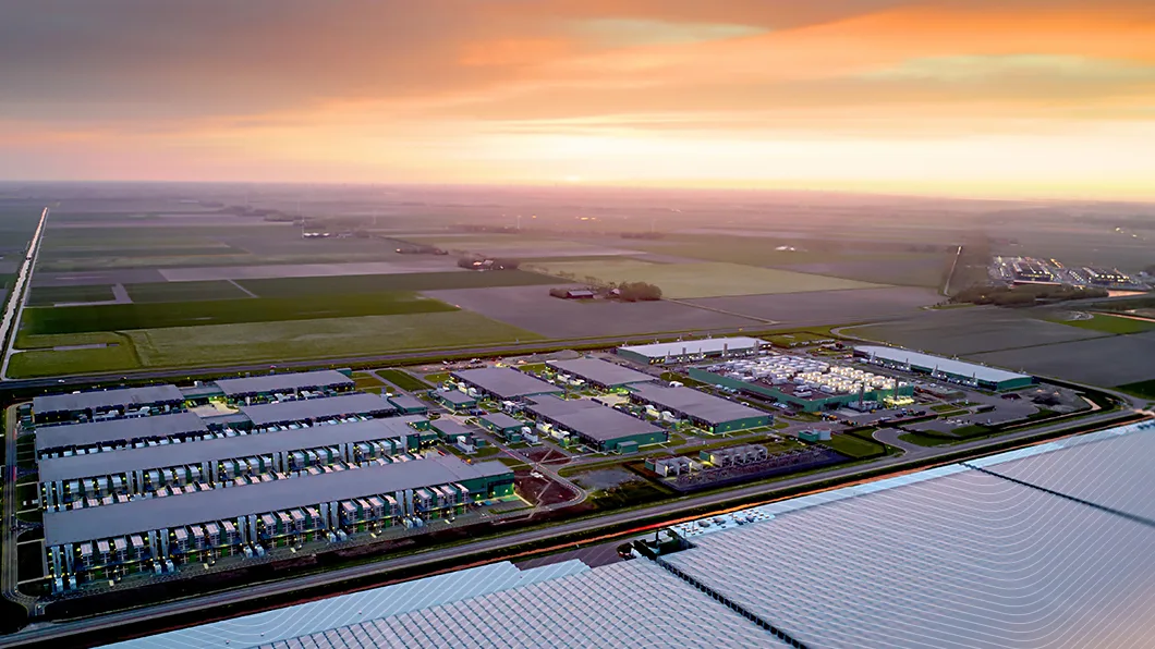 Aerial view of a large data center surrounded by fields at sunset, with vibrant orange and pink sky.