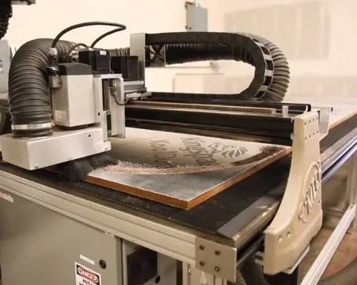 A CNC router machine is carving a pattern into a piece of wood.