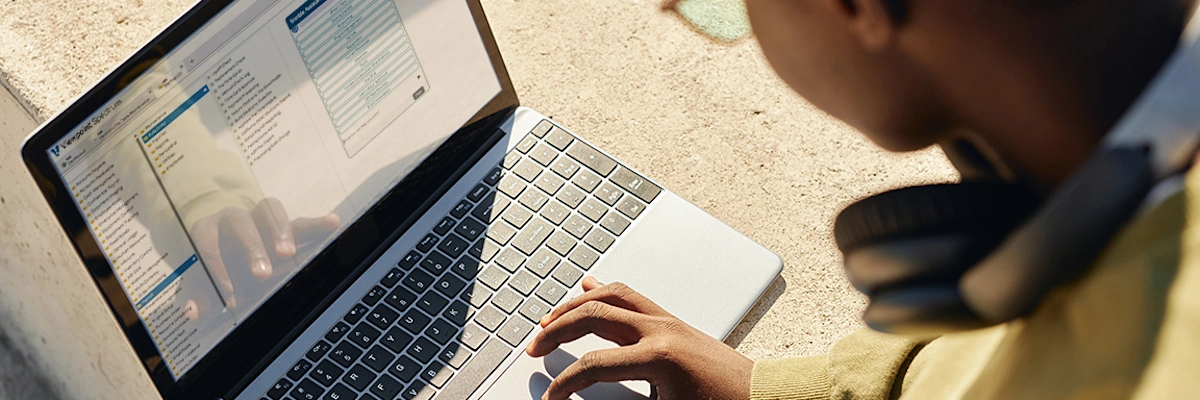 Student with headphones using a laptop outdoors in sunlight.