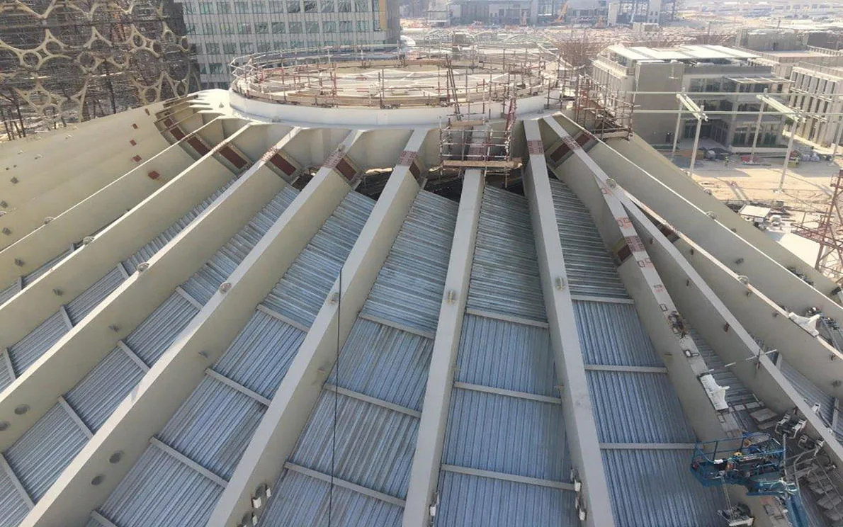 Construction of a large, geodesic-style dome roof with exposed steel beams and corrugated metal sheeting.