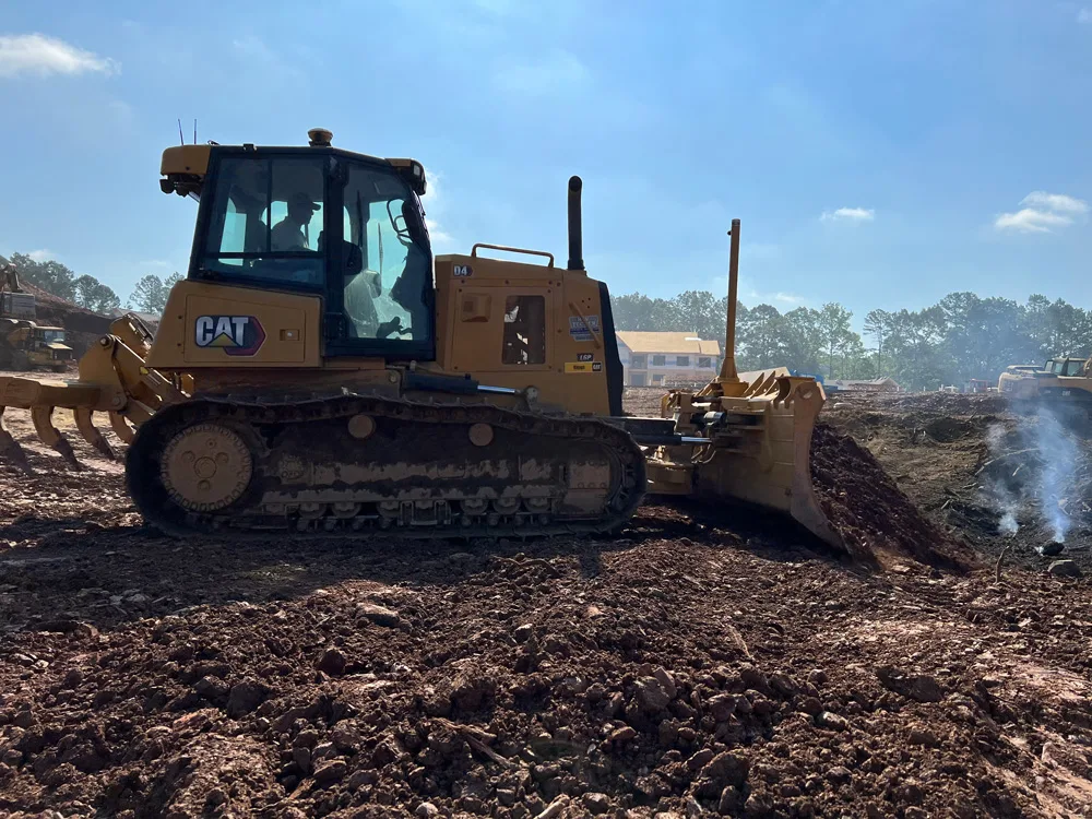 Yellow Caterpillar bulldozer operating on a construction site, clearing dirt with its blade.