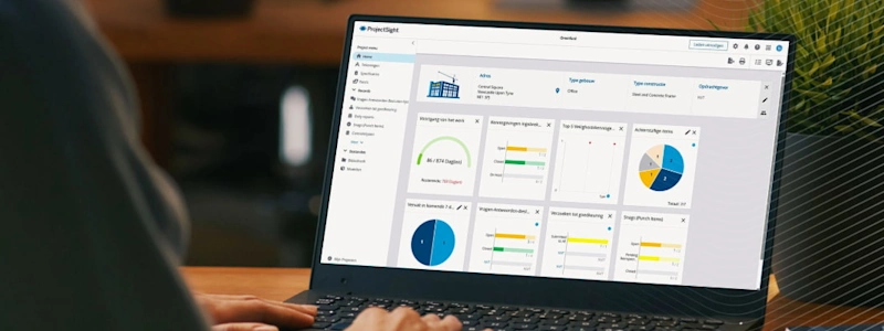 Op een laptopscherm wordt het ProjectSight-dashboard weergegeven met gegevens en grafieken over bouwprojecten.