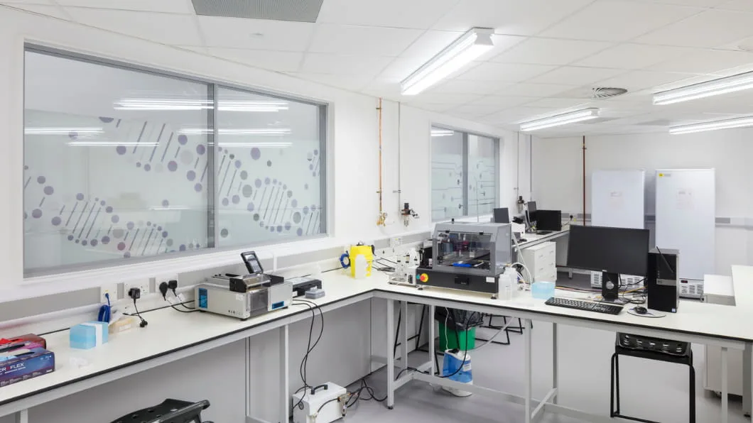 Clean laboratory with white benches, tech equipment, and DNA double-helix decals on the windows.