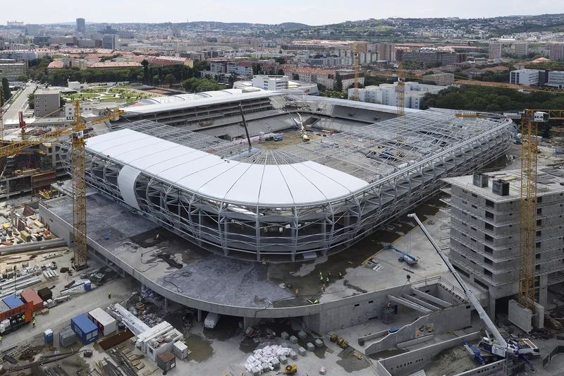 Aerial view of a stadium under construction, with cranes and building materials visible on site.