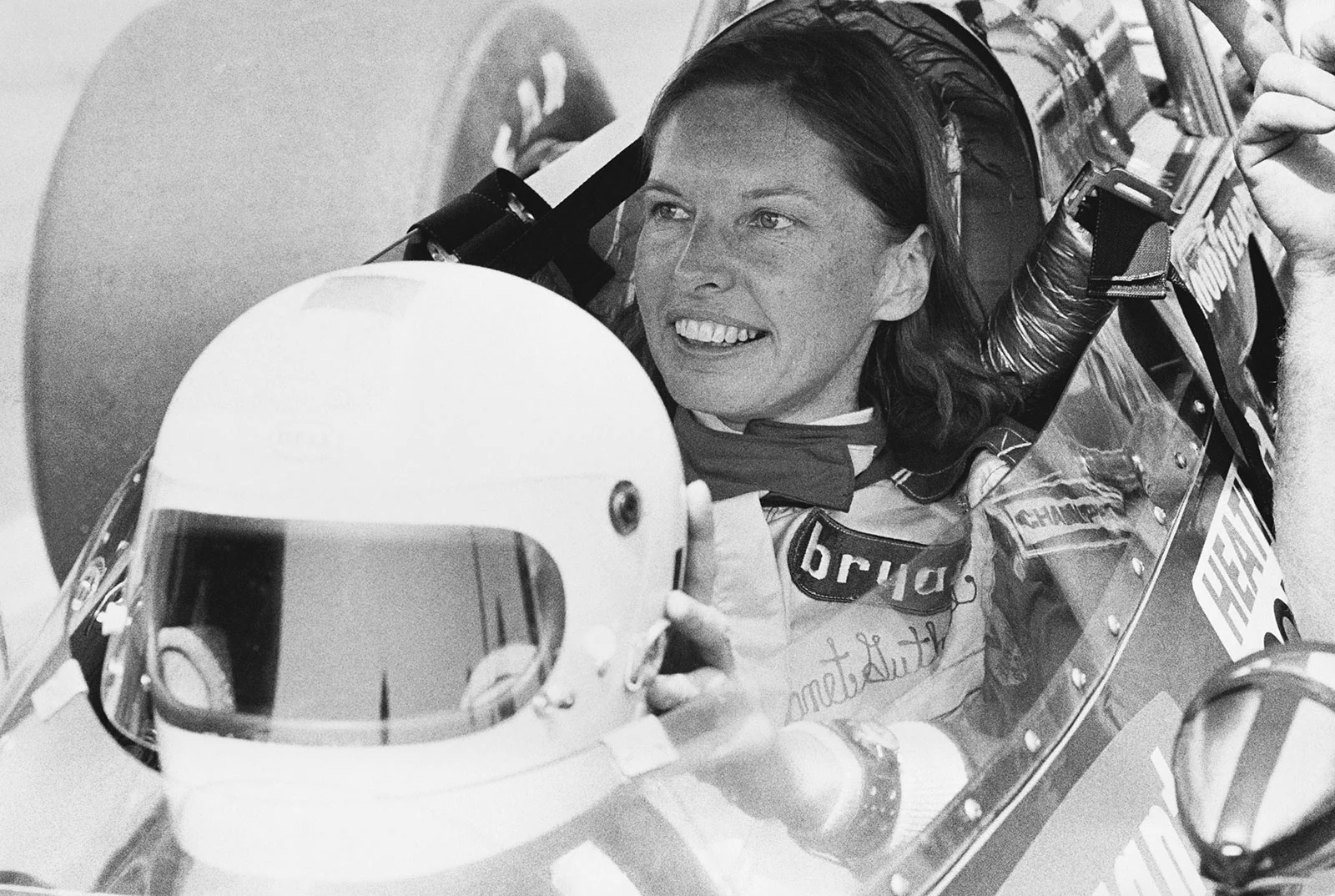 Shirley Muldowney in her race car, holding her helmet.