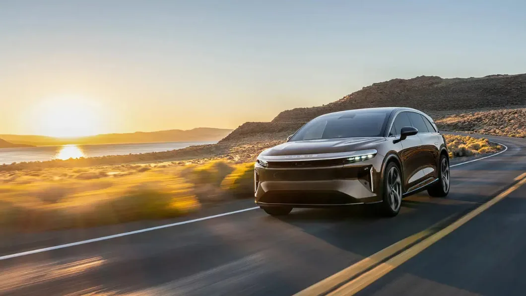 A Lucid Gravity SUV drives along a winding coastal highway at sunset.