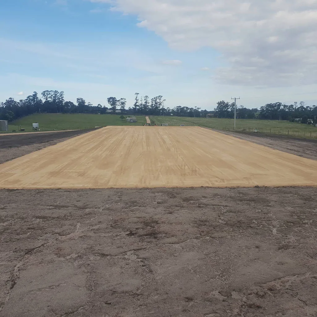 A large, flat, sand-covered area is prepared for construction under a cloudy blue sky.
