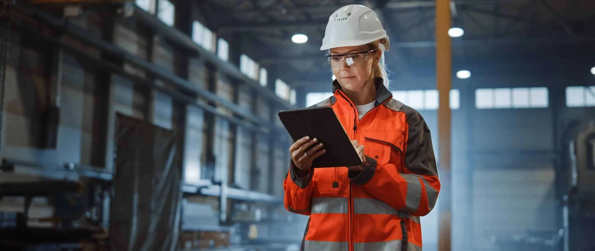 Worker in safety gear using a tablet in a factory.
