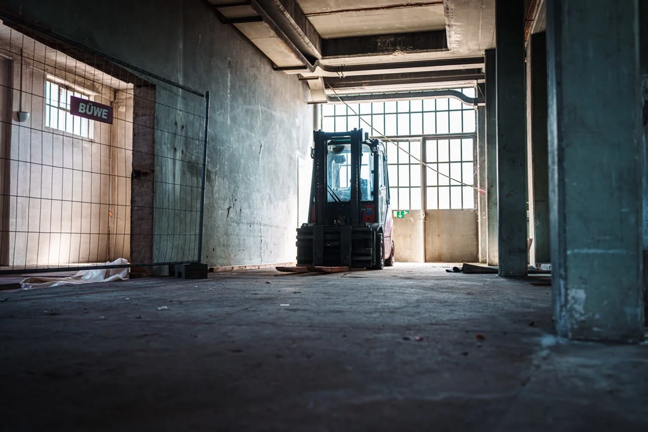 Forklift in a large, empty industrial space with concrete walls and large windows.