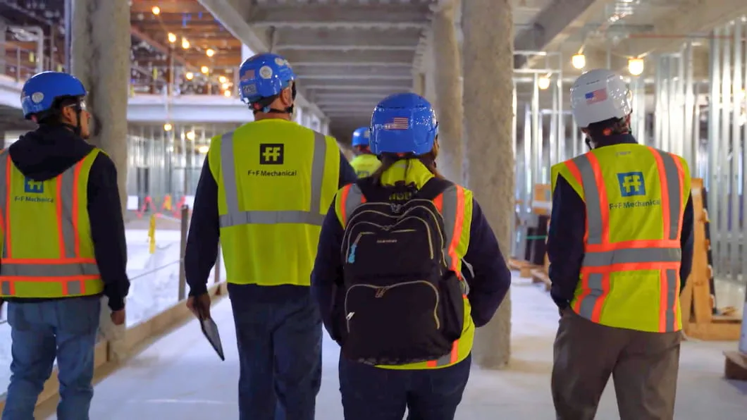 A team of four workers in F+F Mechanical safety gear walks through an indoor construction site.
