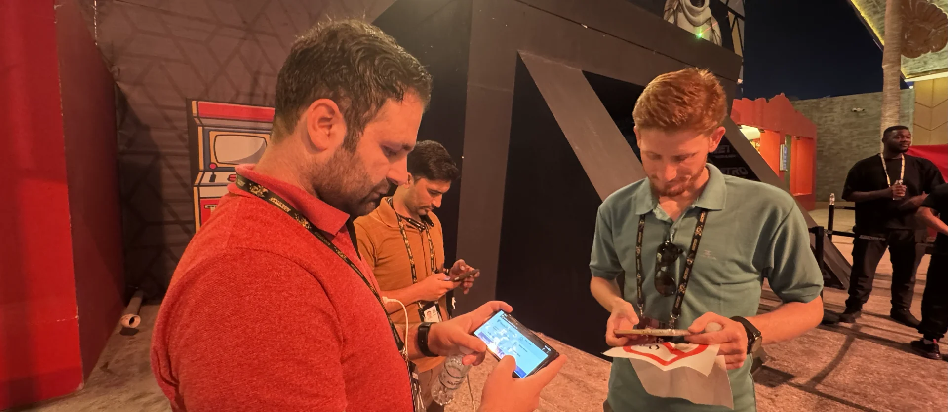 Two men in casual attire are using Viewpoint Field View on phones at the Esports World Cup