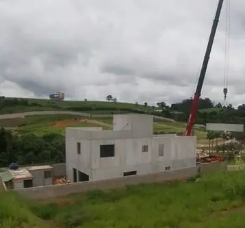 A concrete house is under construction on a grassy hill, with a large crane extending over the scene.