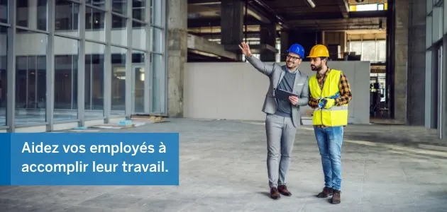 Two construction workers are looking at a blueprint in a large, unfinished building.