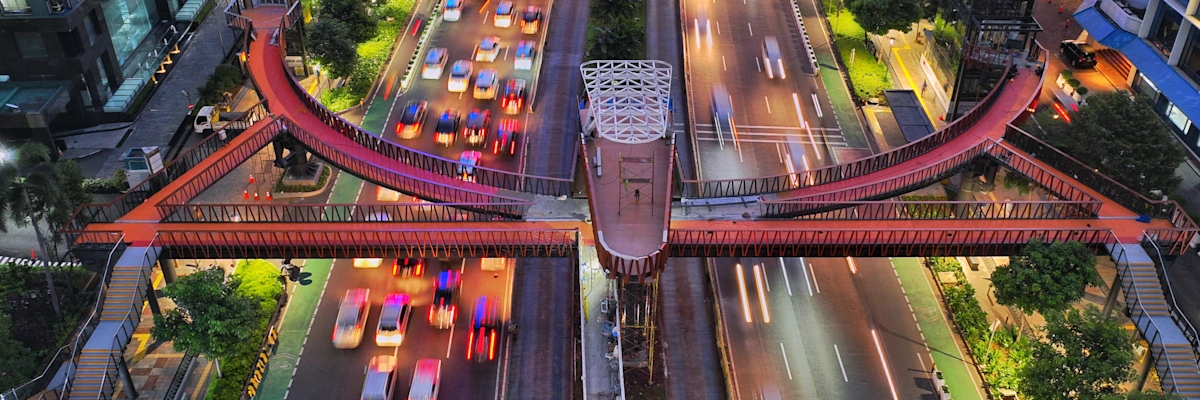The Pinisi Bridge at night above ongoing traffic and buildings.