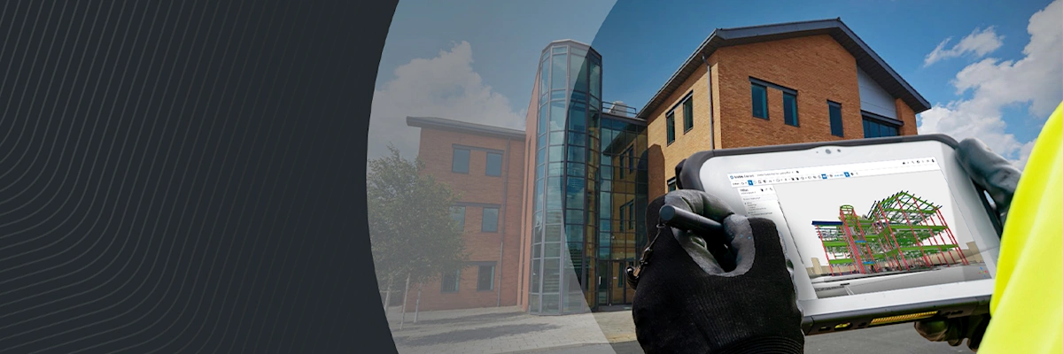 A person in a high-vis vest uses a tablet to view a 3D structural model in front of a modern brick building.