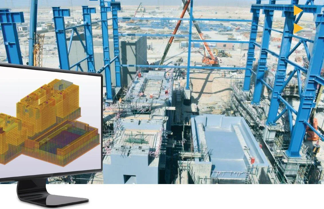 A computer monitor displays a 3D model of a building complex, superimposed over a real-life construction site of a large industrial facility.