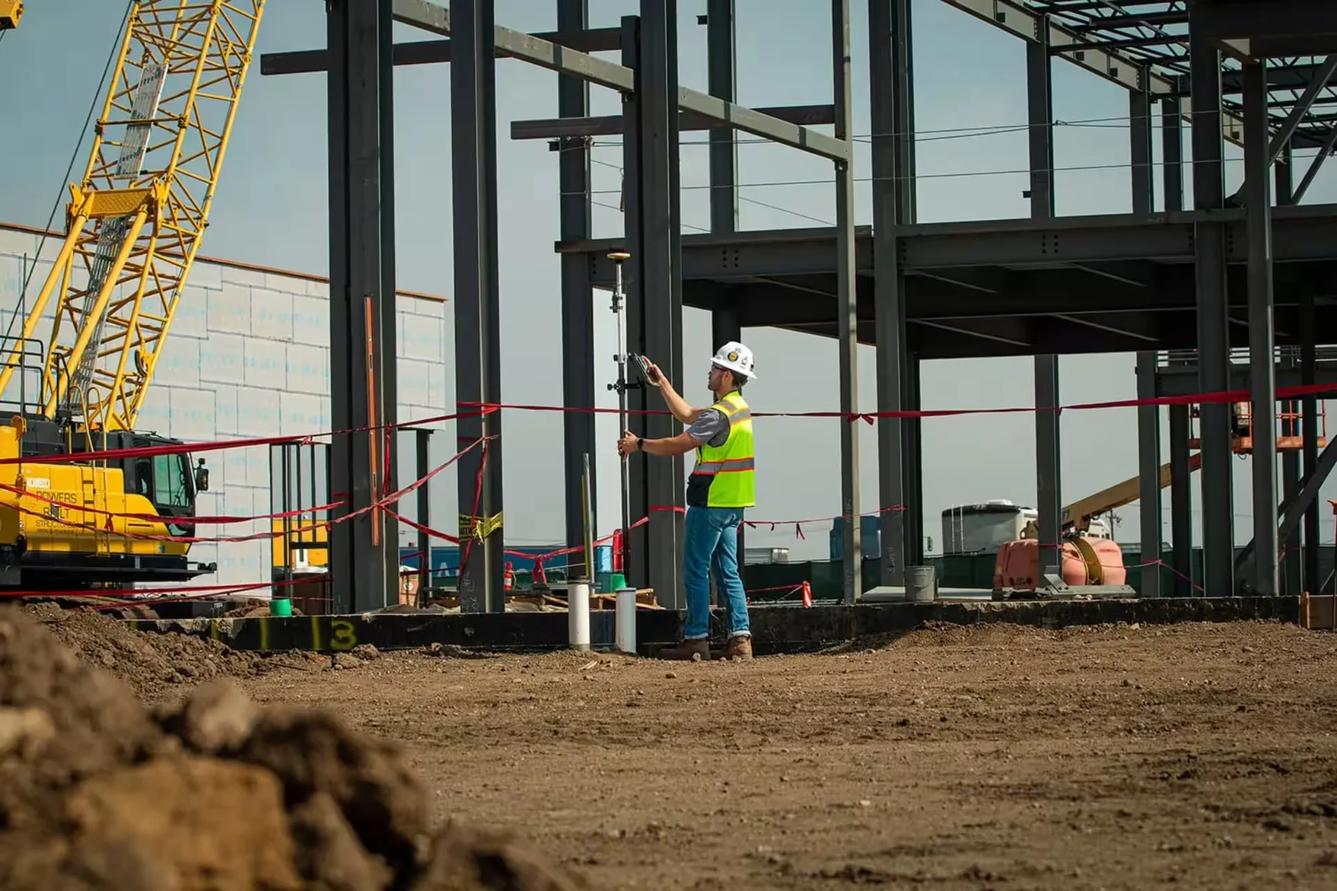 Surveyor uses equipment on a construction site with a crane in the background.