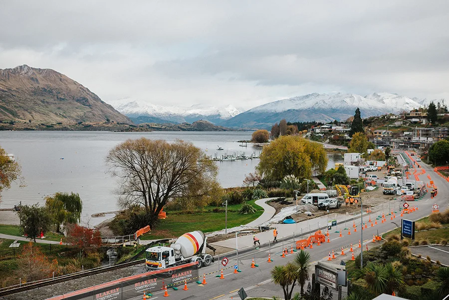 Construction on a road next to a lake, with mountains in the background.