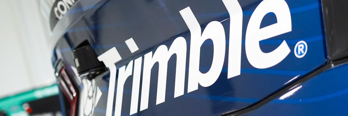 Trimble logo on a blue vehicle featuring a side-mounted camera sensor, with a CONEXPO-CON/AGG trade show decal visible in the background.