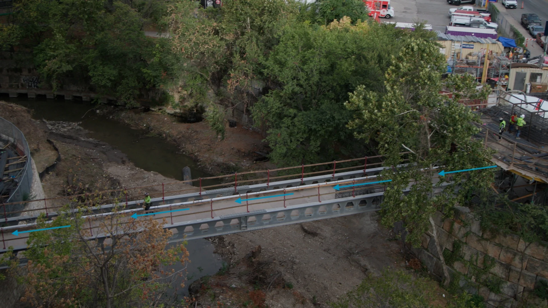 Construction workers are seen on a bridge over a dry creek bed.