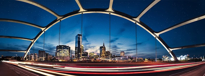 Nashville, TN skyline at night, framed by Korean War Veterans Memorial Bridge. Vehicle light trails pass, highlighting the illuminated AT&T "Batman Building".