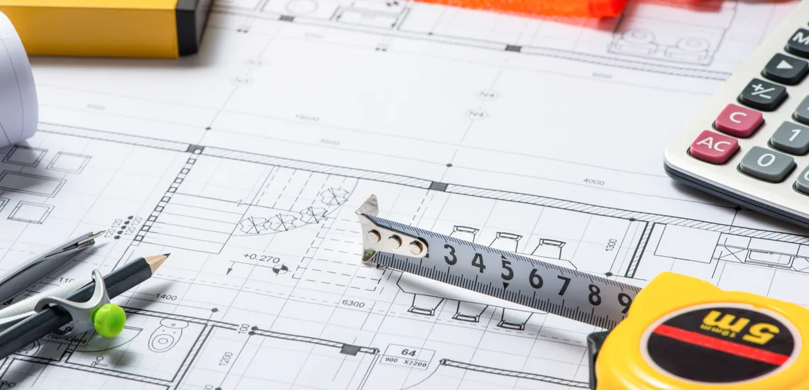 Architectural blueprint with a tape measure, calculator, and drafting tools, indicating a workspace for design and planning