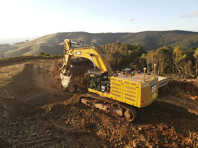 A large yellow CAT excavator moves dirt on a construction site.