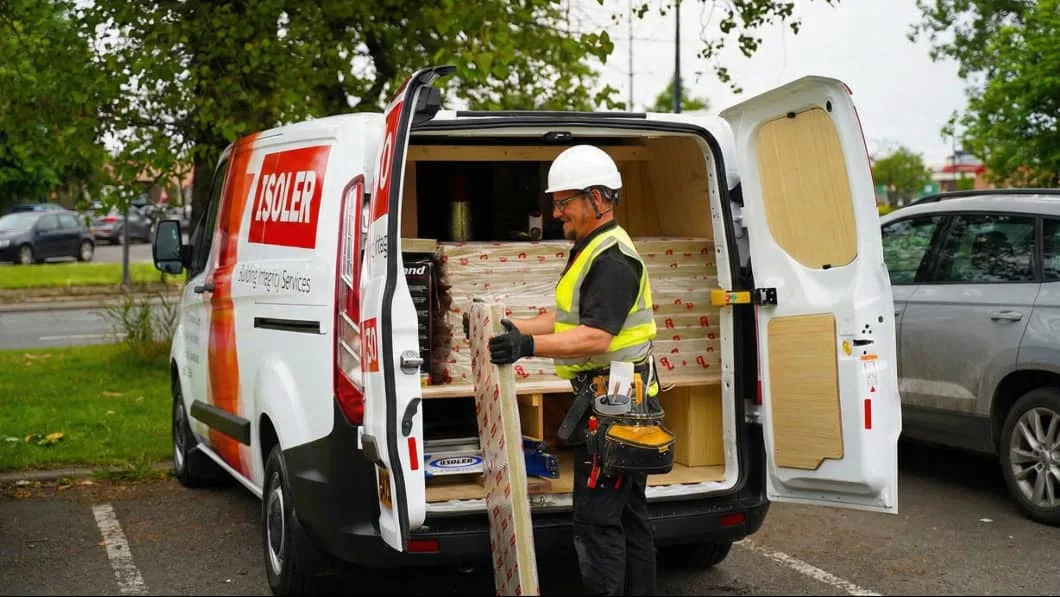Construction worker in safety gear unloading insulation materials from a white ISOLER company van.