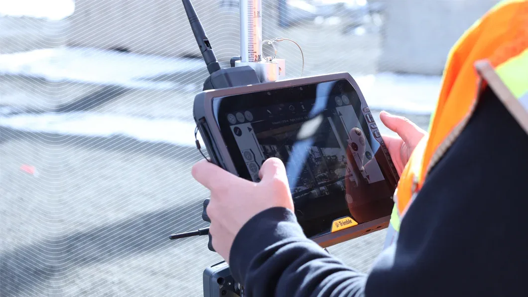 A surveyor uses a Trimble T100 rugged tablet on a surveying rod to manage construction data on an outdoor site.