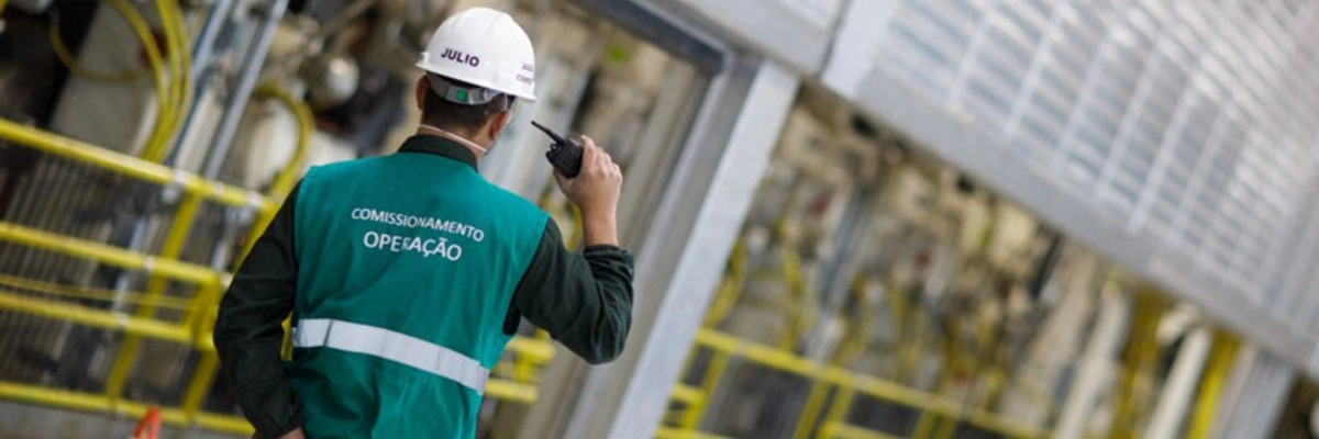 Klabin employee in a green vest and white hard hat using a walkie-talkie at at the company's PUMA Unit in Ortigueira, Paraná.