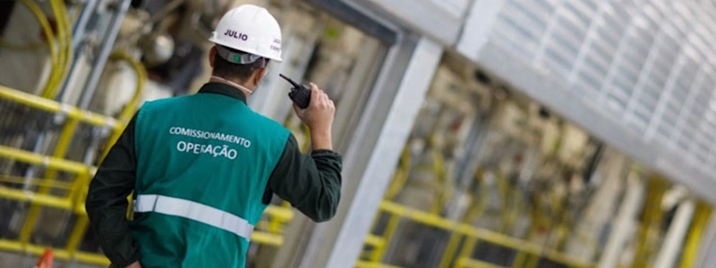 Klabin employee in a green vest and white hard hat using a walkie-talkie at at the company's PUMA Unit in Ortigueira, Paraná.