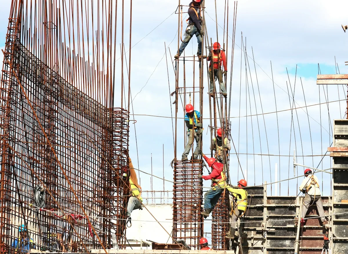 Construction workers in red and yellow hard hats assemble rebar for a high-rise building.